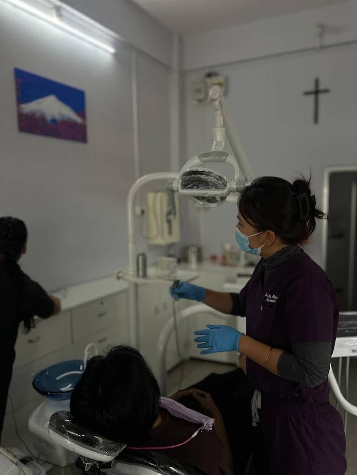 Dentist wearing purple scrubs and blue gloves treats a patient in a dental office.